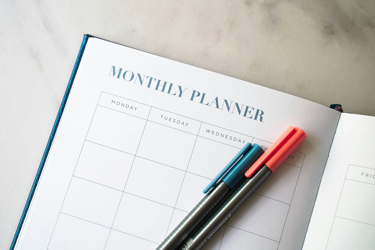 An open monthly planner and pens on a cream-colored surface